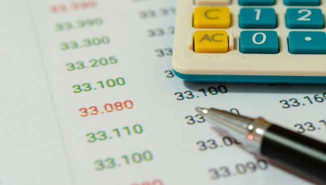 Uma calculadora e uma caneta posicionadas sobre um documento financeiro, representando planejamento e gestão de estatísticas do leite..